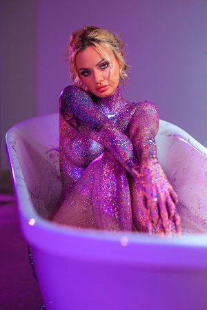 Female model posting in a claw foot bathtub covered in purple glitter