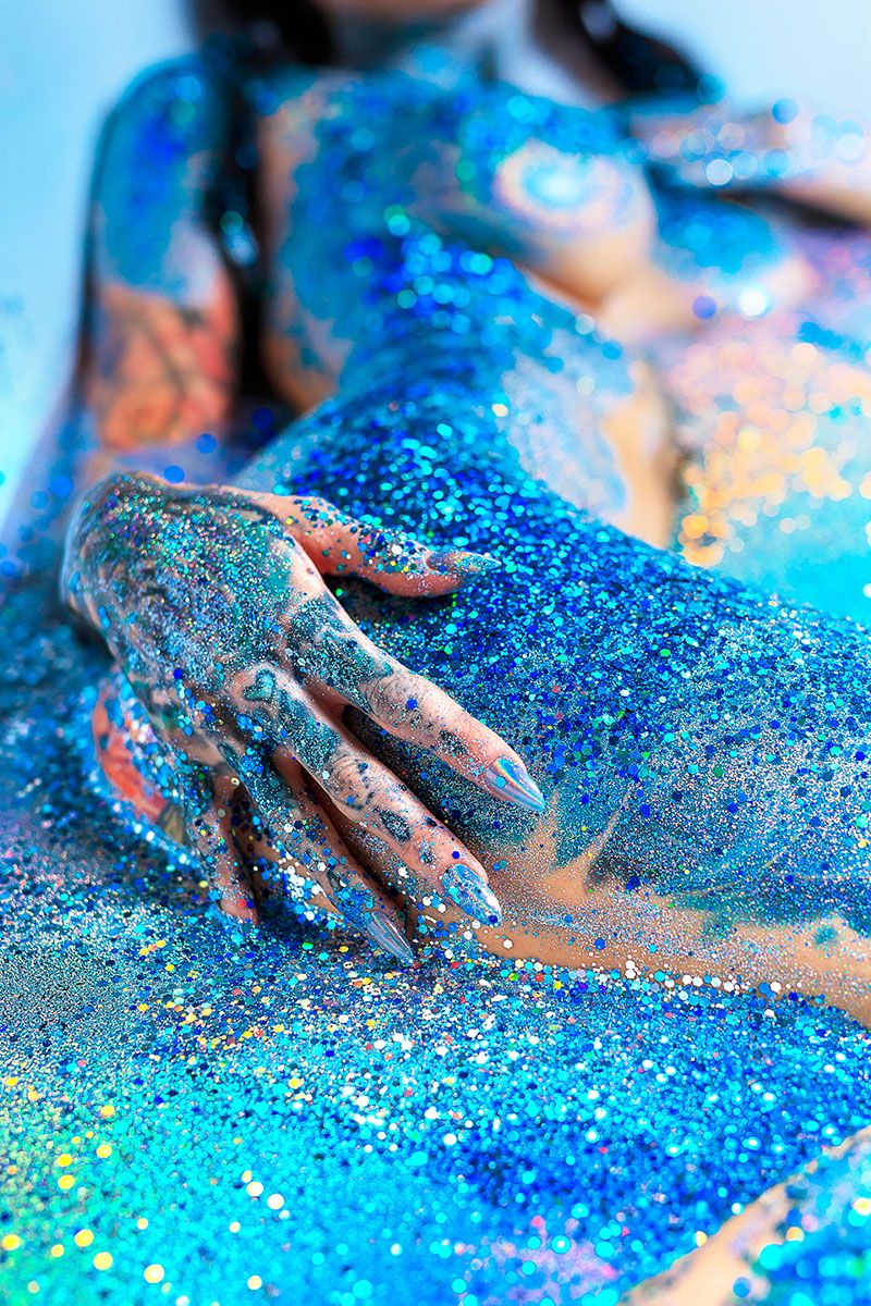 Female model posting in a claw foot bathtub covered in blue glitter