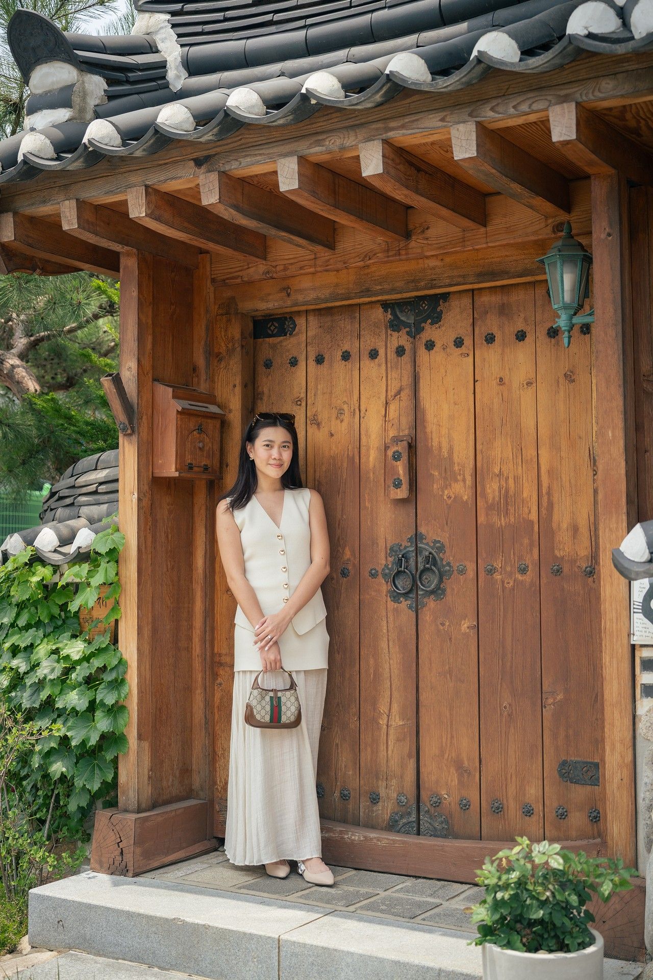 A person in traditional Korean hanbok dress stands in front of a rustic wooden door at a traditional Korean hanok house.