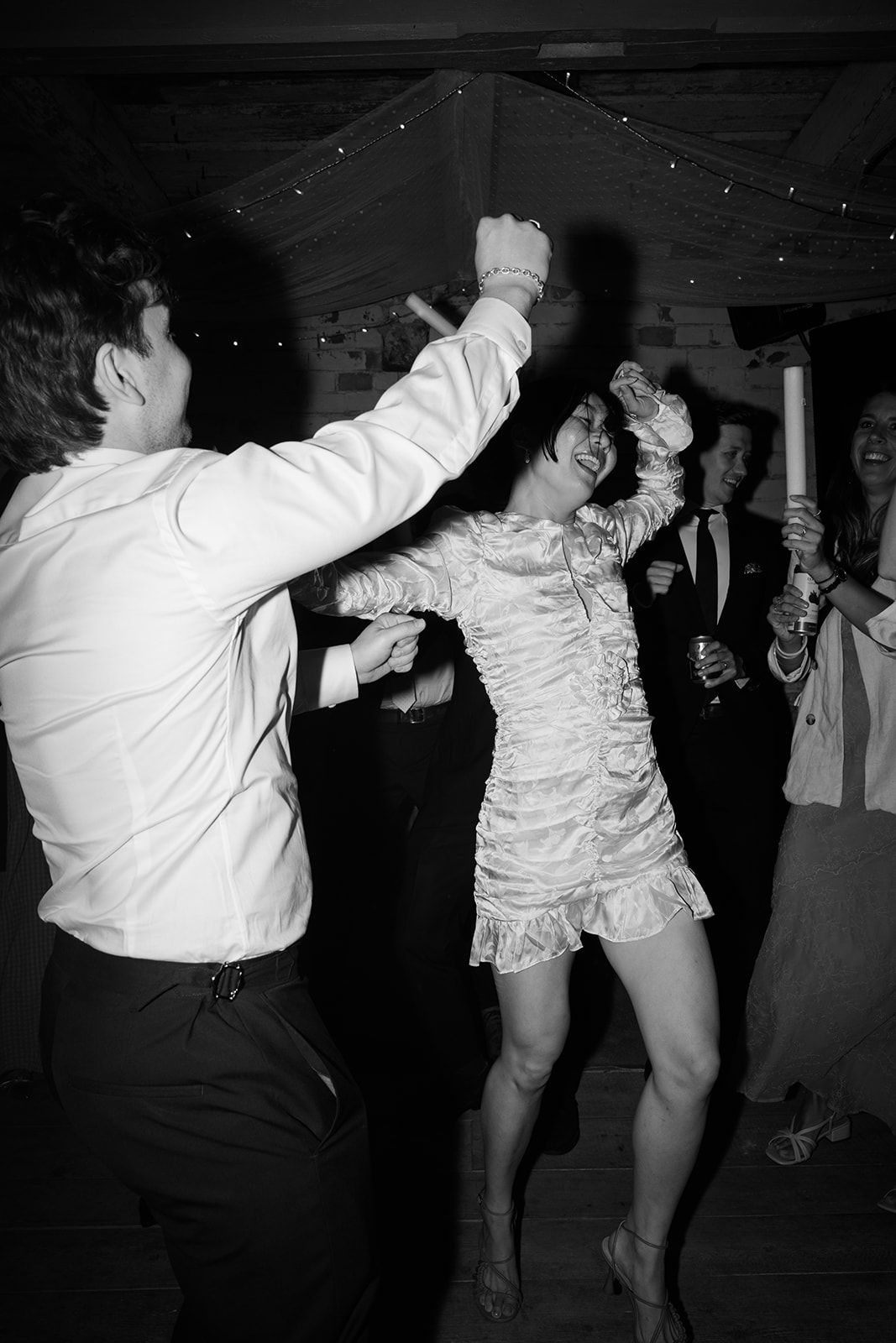 Black and white sequence of two people dancing energetically at a party with dramatic movements and white clothing.
