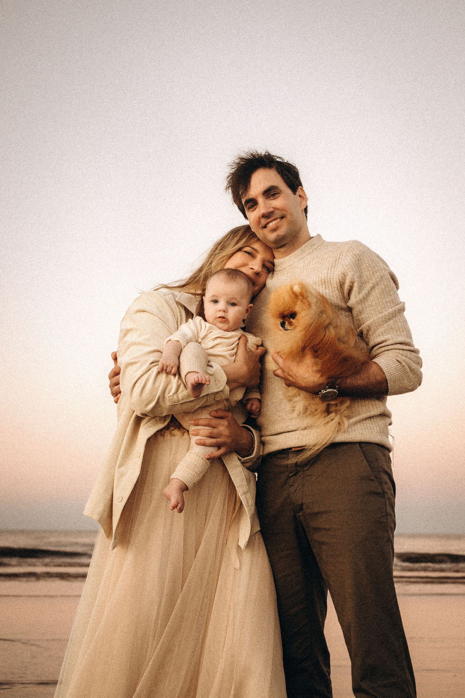 A family shares tender moments with their baby on a serene beach at sunset in matching cream and brown tones. Javea photographer