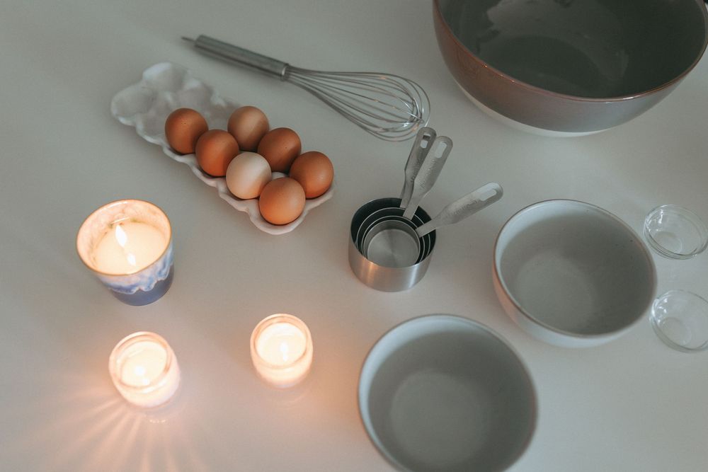 Cooking ingredients and utensils arranged on white surface with brown eggs and mixing bowls.