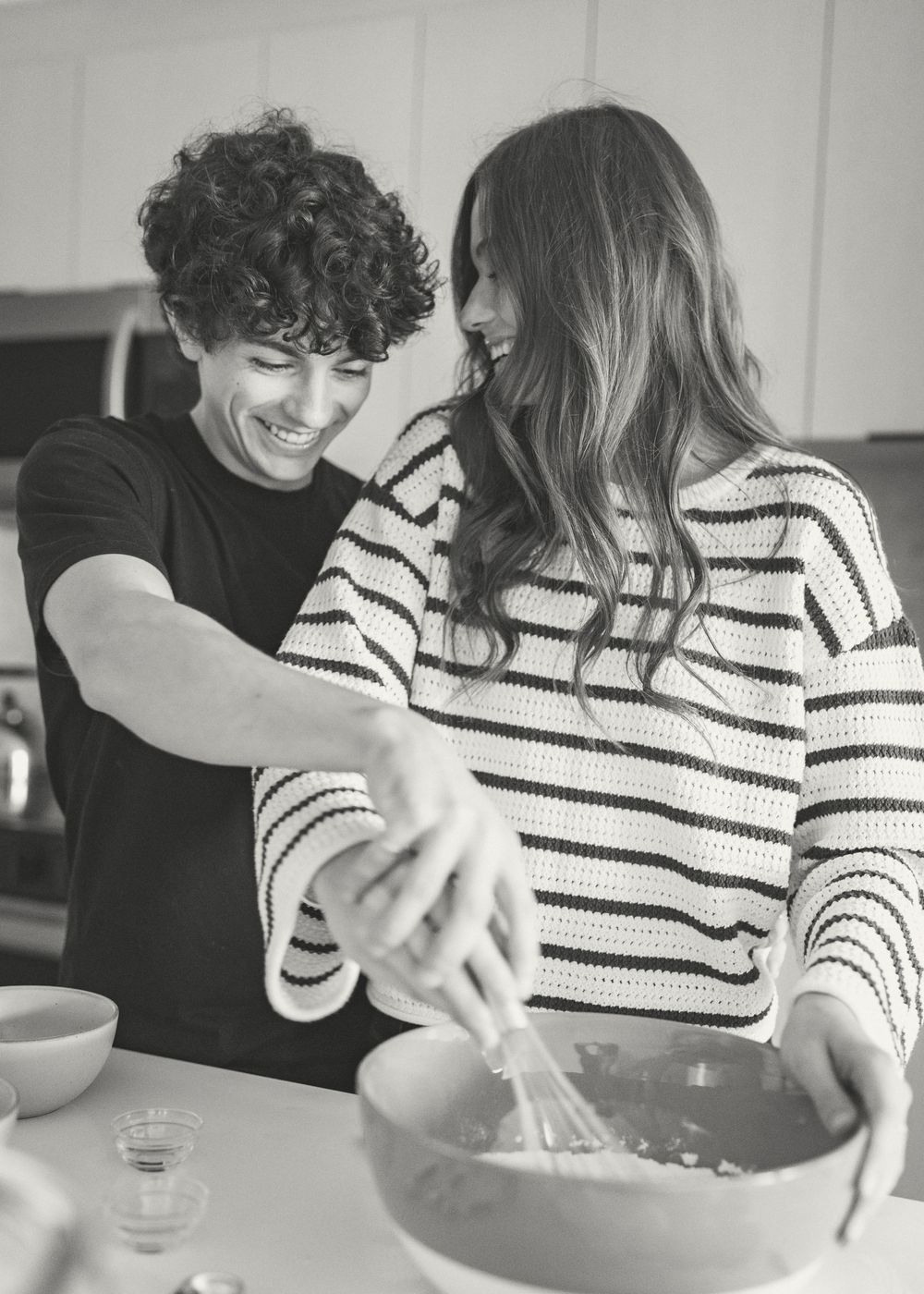 Two people cooking together while sharing affectionate moments in a bright kitchen.