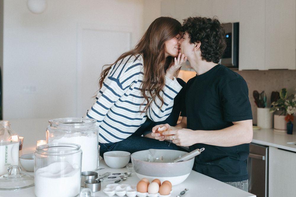 Two people playfully baking together in a minimalist white kitchen.