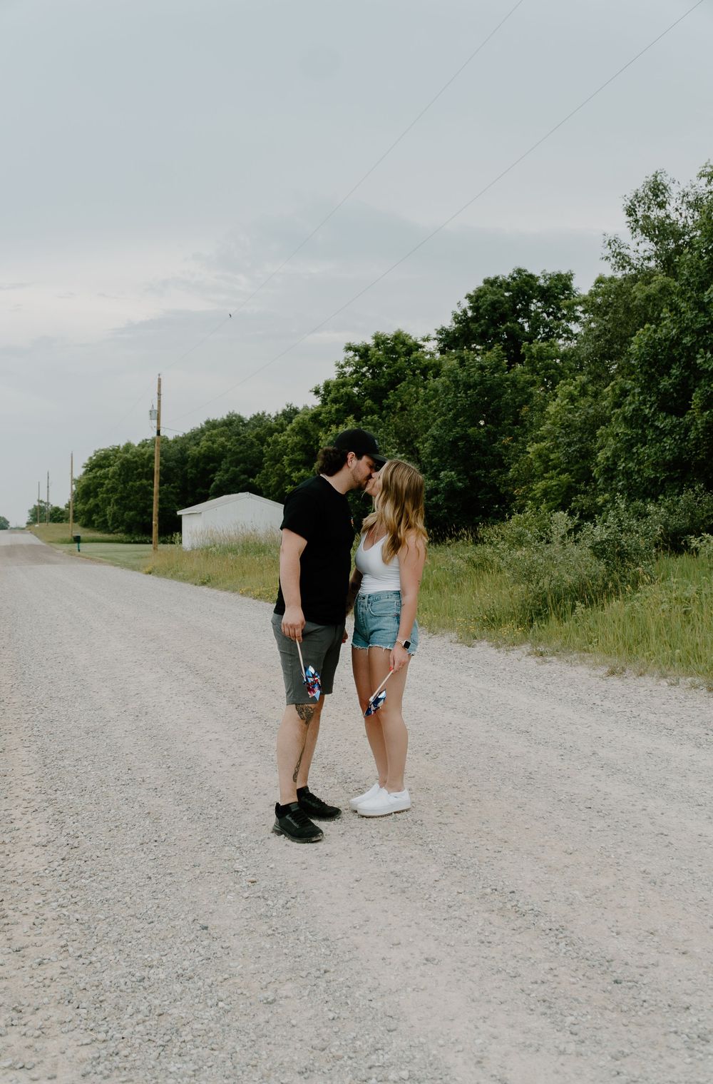 Two people share a tender moment on a gravel path surrounded by green vegetation on a cloudy day.