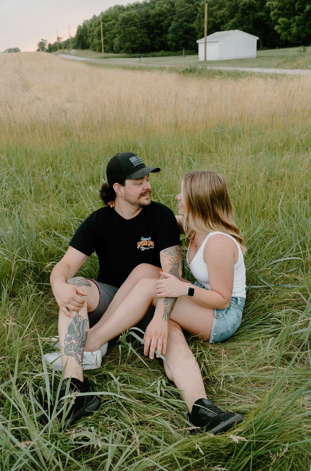 A couple sits together in tall grass on a summer evening having an intimate conversation.