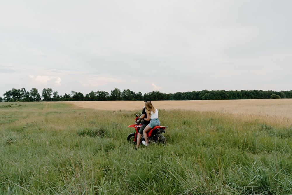 A couple sits together in a vast green prairie field during golden hour.