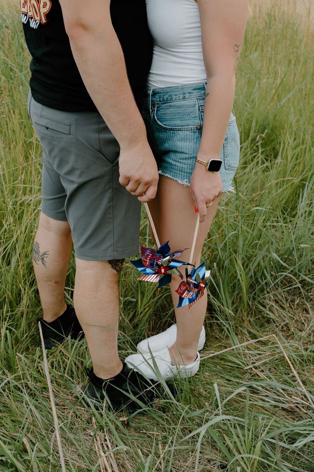 Close-up view of legs and feet standing in tall grass, showing casual summer attire and sneakers.