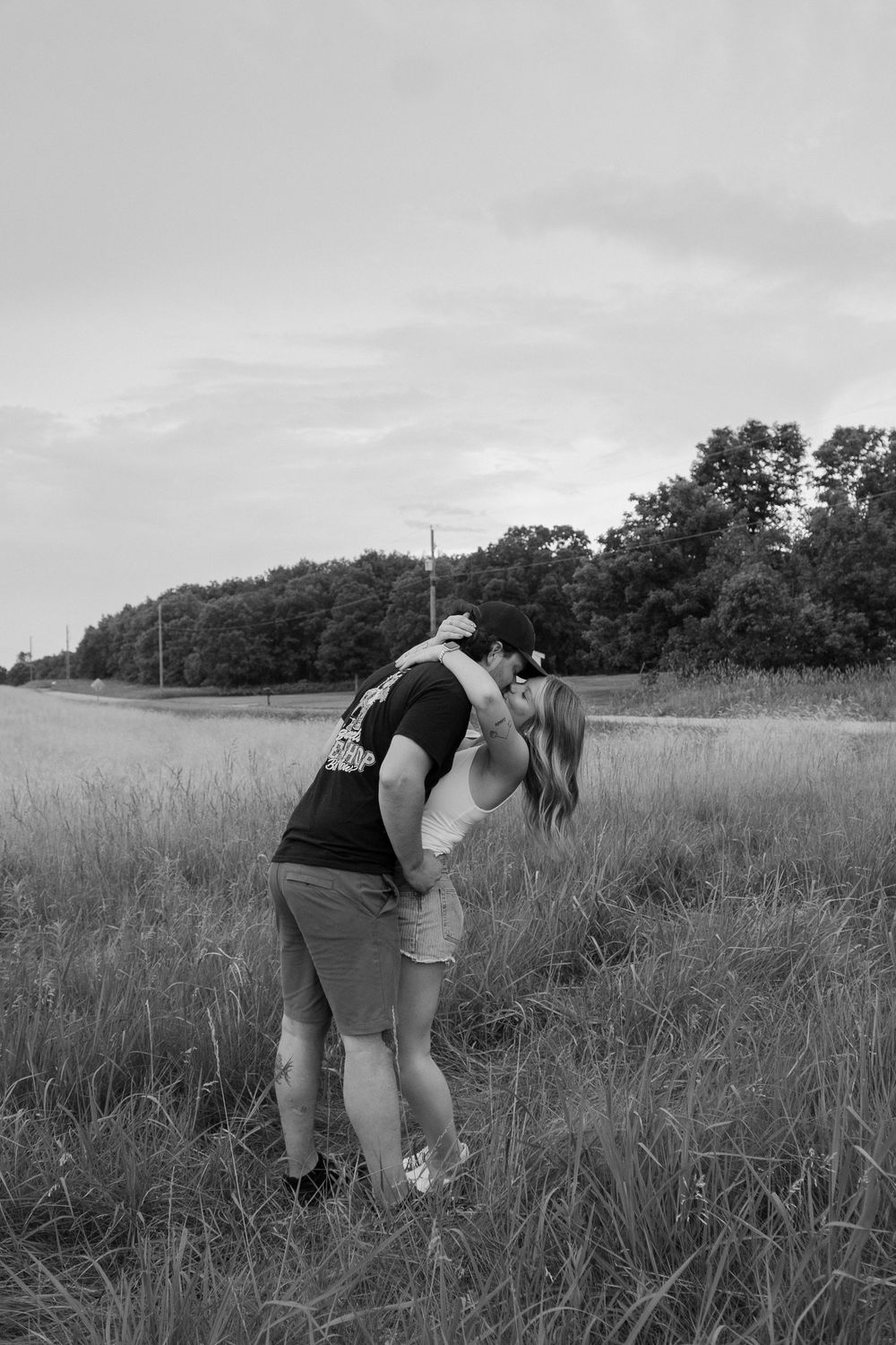 Two people bend down to examine or collect something in a grassy meadow on an overcast day.