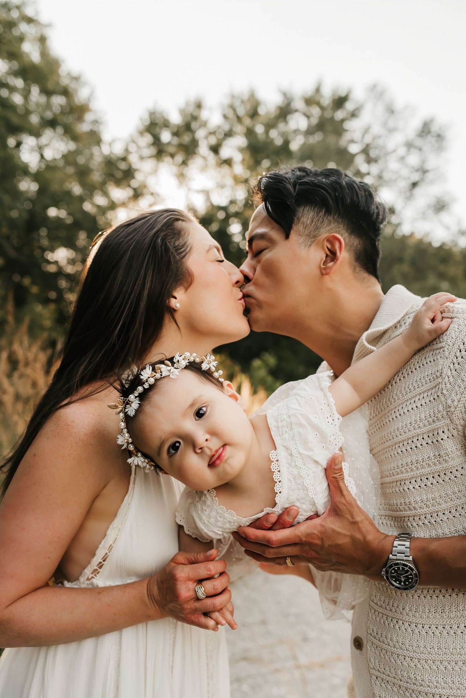 Mom and Dad kiss as they snuggle with their one year old during one year old birthday photo session.