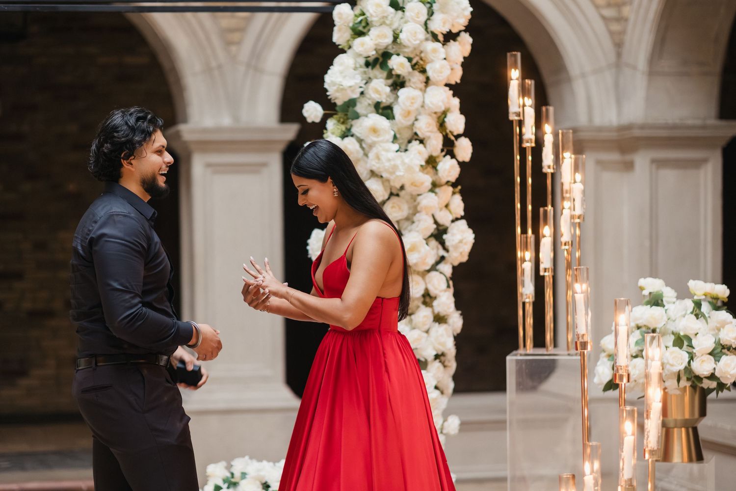 A romantic proposal scene unfolds in an elegant venue decorated with white floral arrangements and glowing candles.