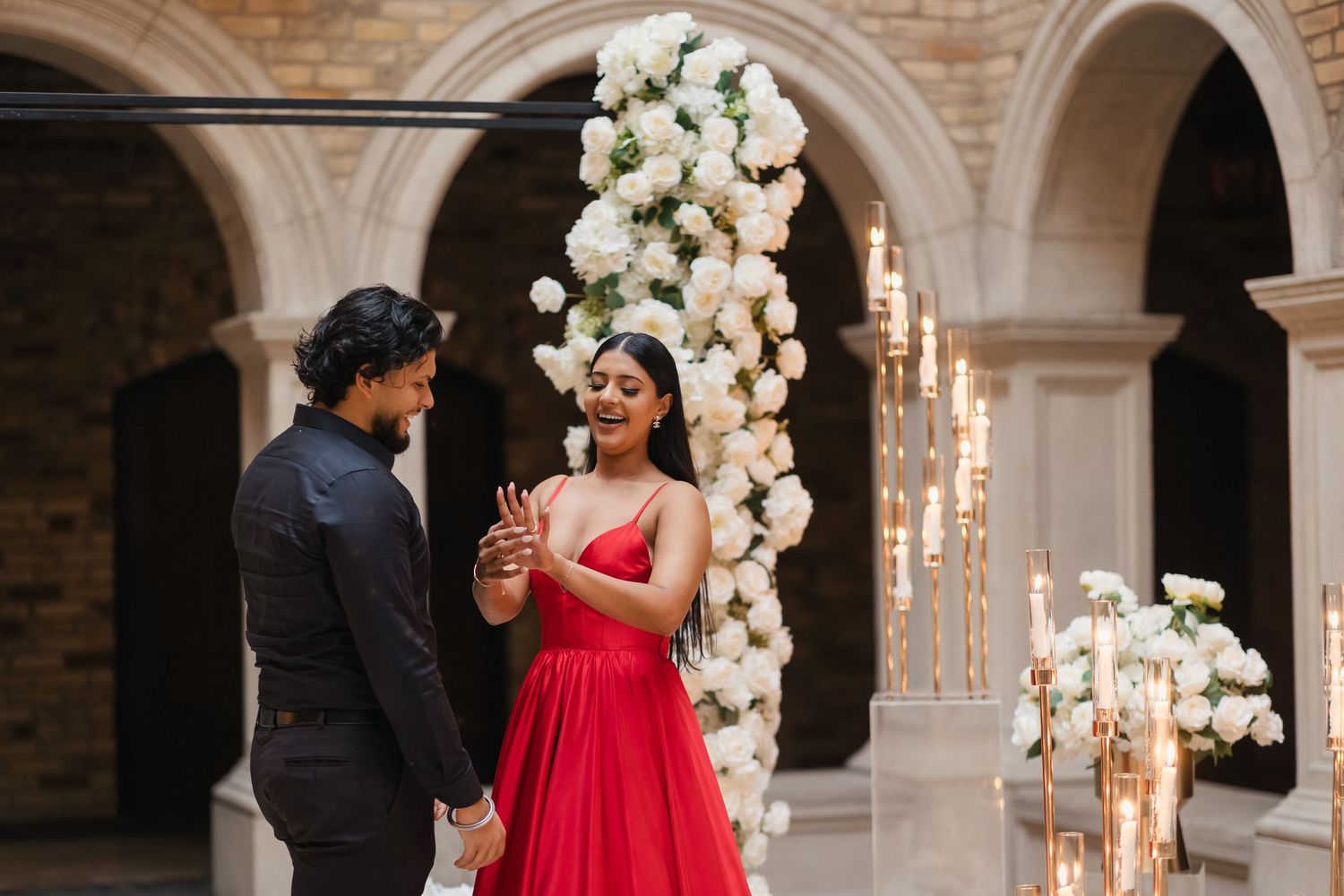 Couple shares an intimate moment in an elegant stone archway venue decorated with white floral arrangements and candles.