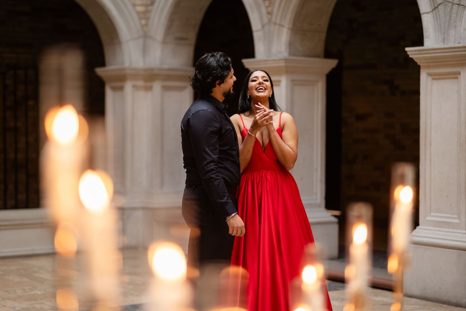 A couple shares an intimate moment in a grand ballroom decorated with elegant white floral arrangements and chandeliers.