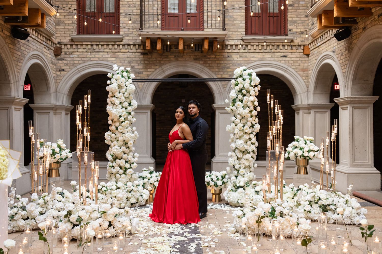 An ornate ballroom features white floral arrangements and classical architecture with arched columns and warm lighting.