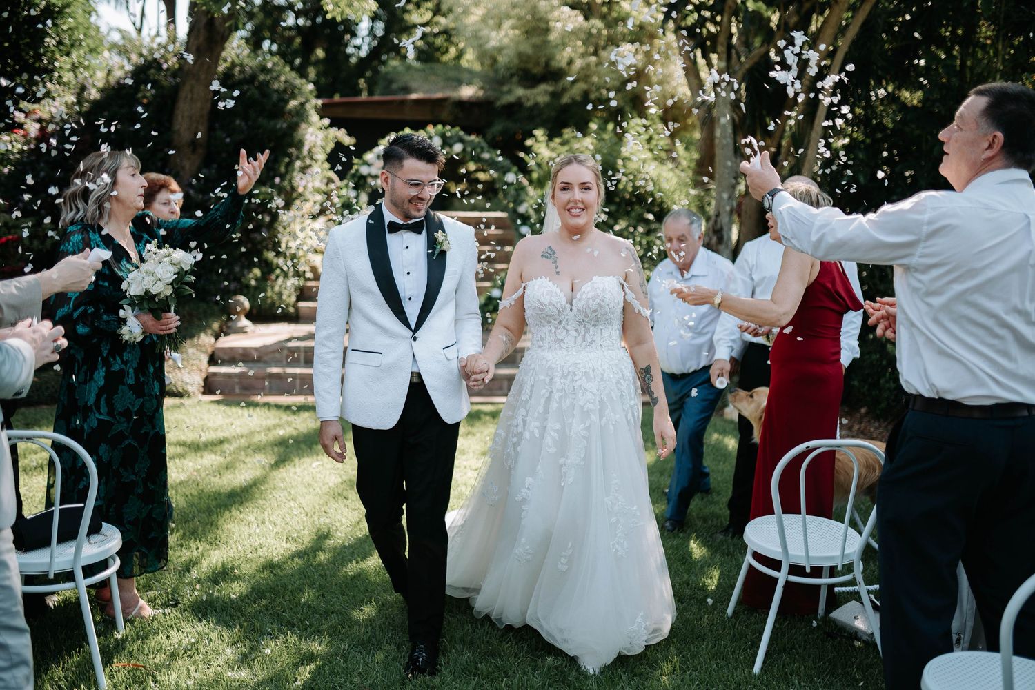 Wedding guests celebrate and dance together during an outdoor garden reception on a sunny afternoon.