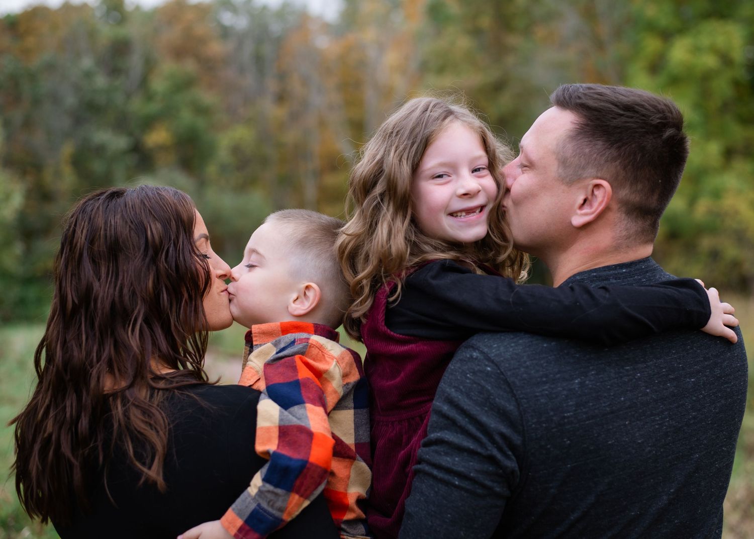 A family shares tender moments together outdoors during an autumn photoshoot in a wooded setting.