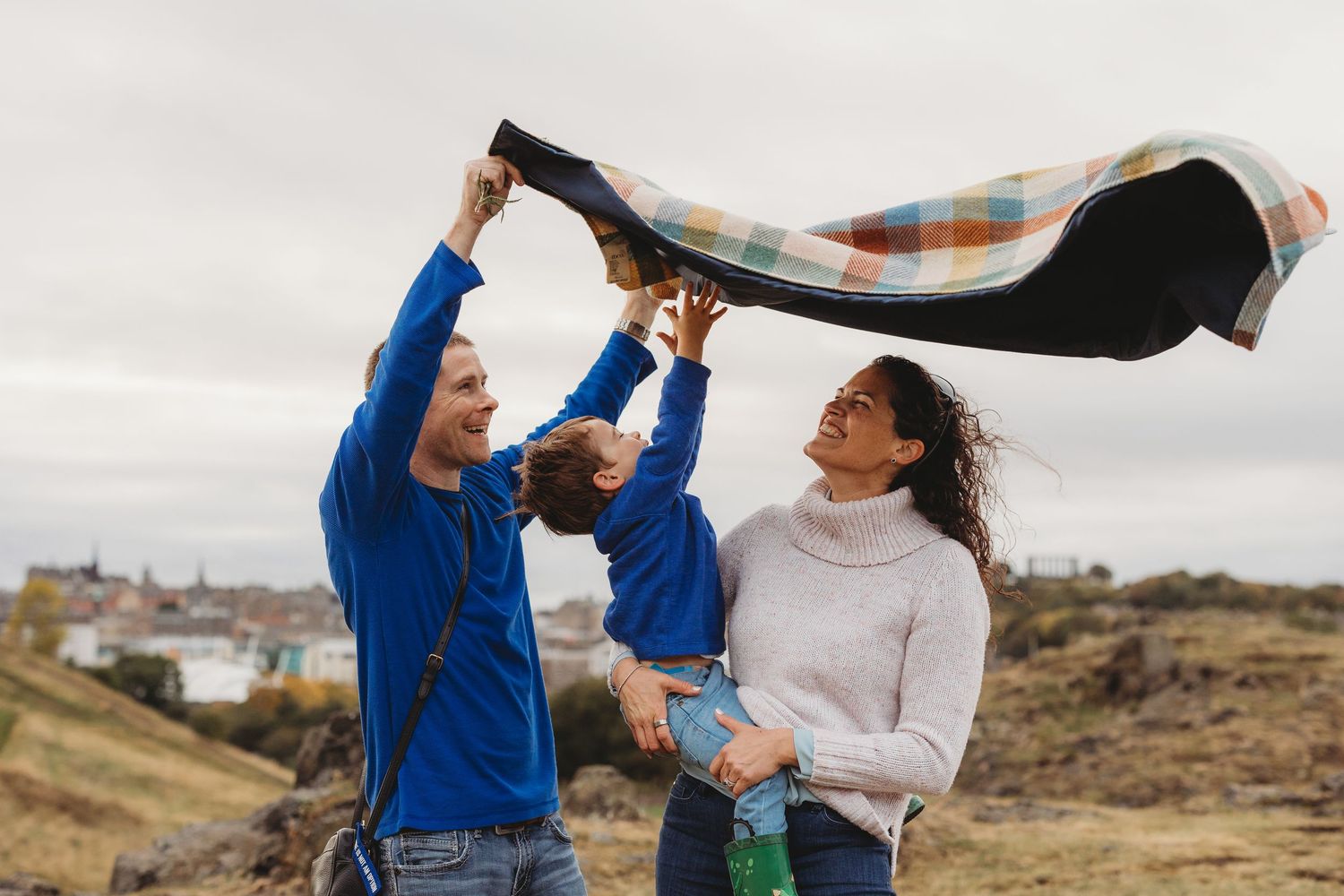 A couple dances together in a field on a cloudy day, with the woman wearing a white jumper and the man in blue. Holding a boy.