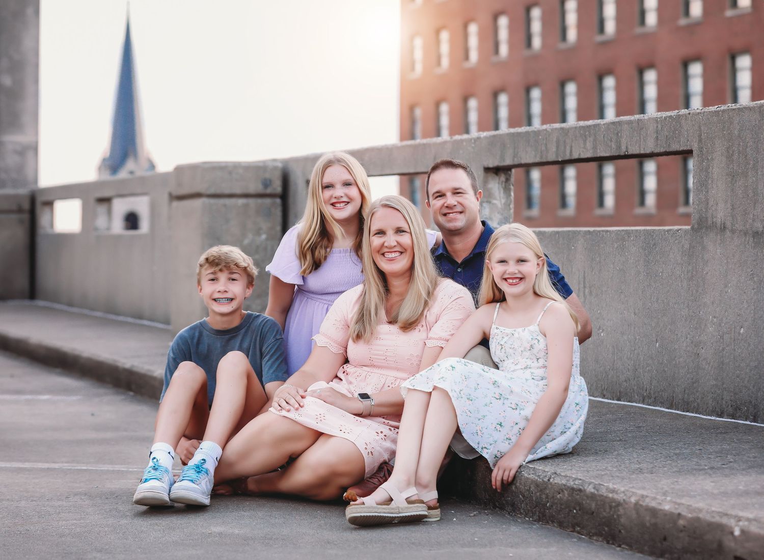 A family enjoys a warm sunset photoshoot in a field with golden light filtering through trees in the background.