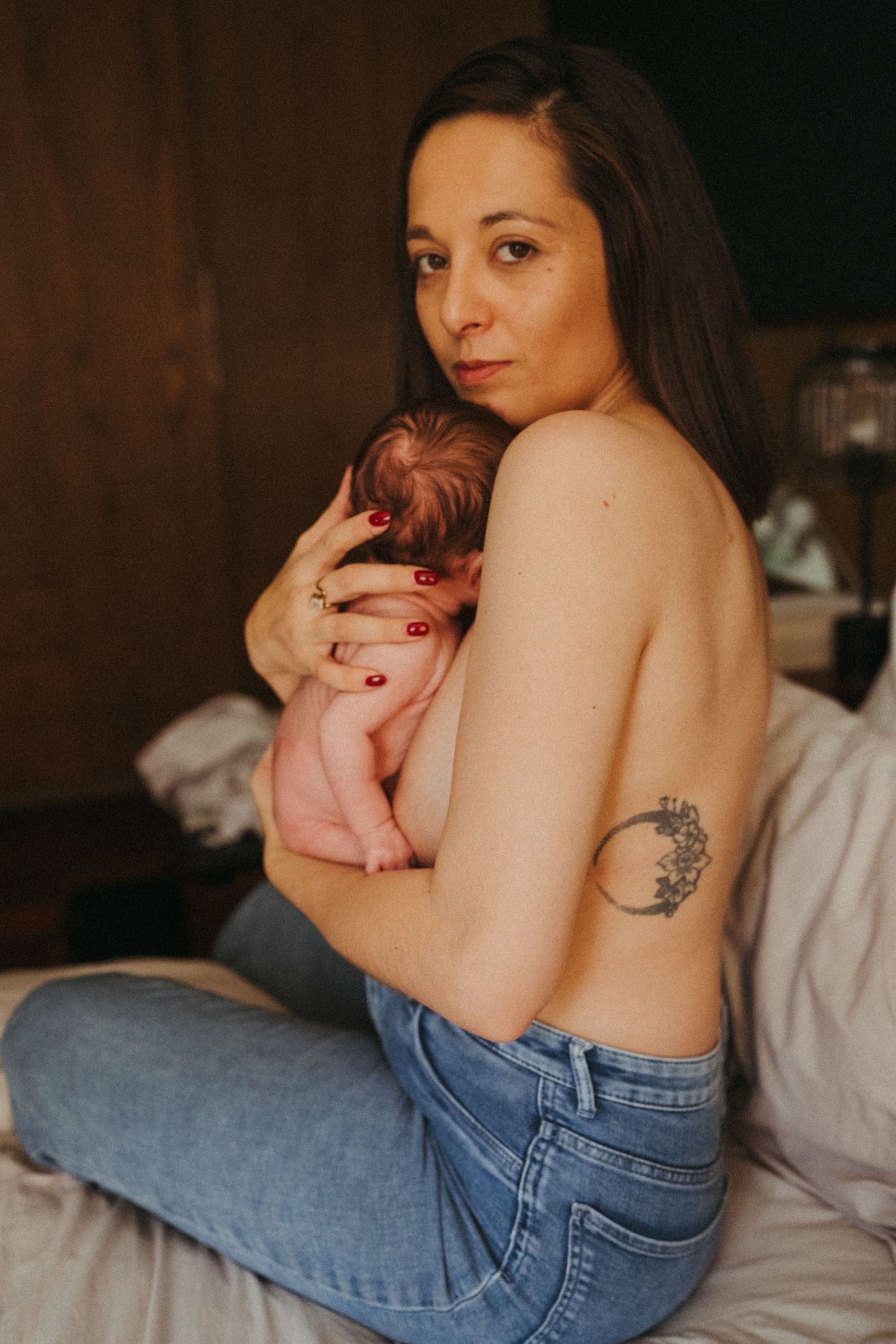 Woman in jeans reclining on white bed with tattoo visible.
