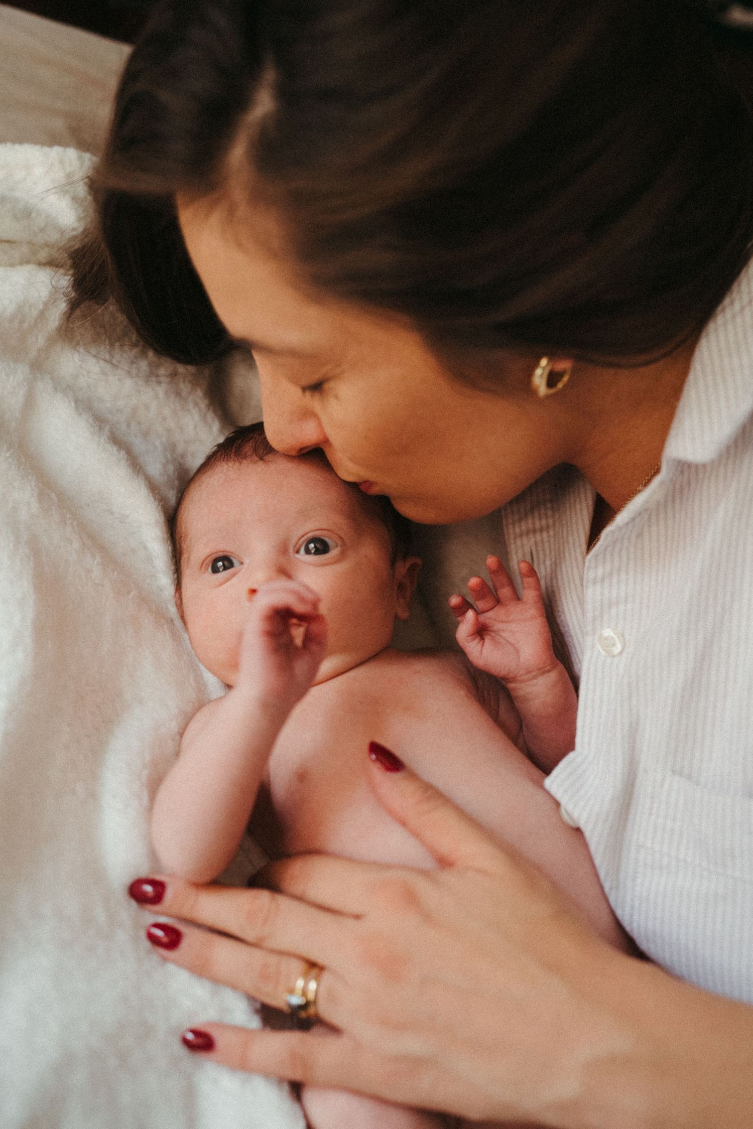 Mother in white shirt sharing tender moment with baby on bed.
