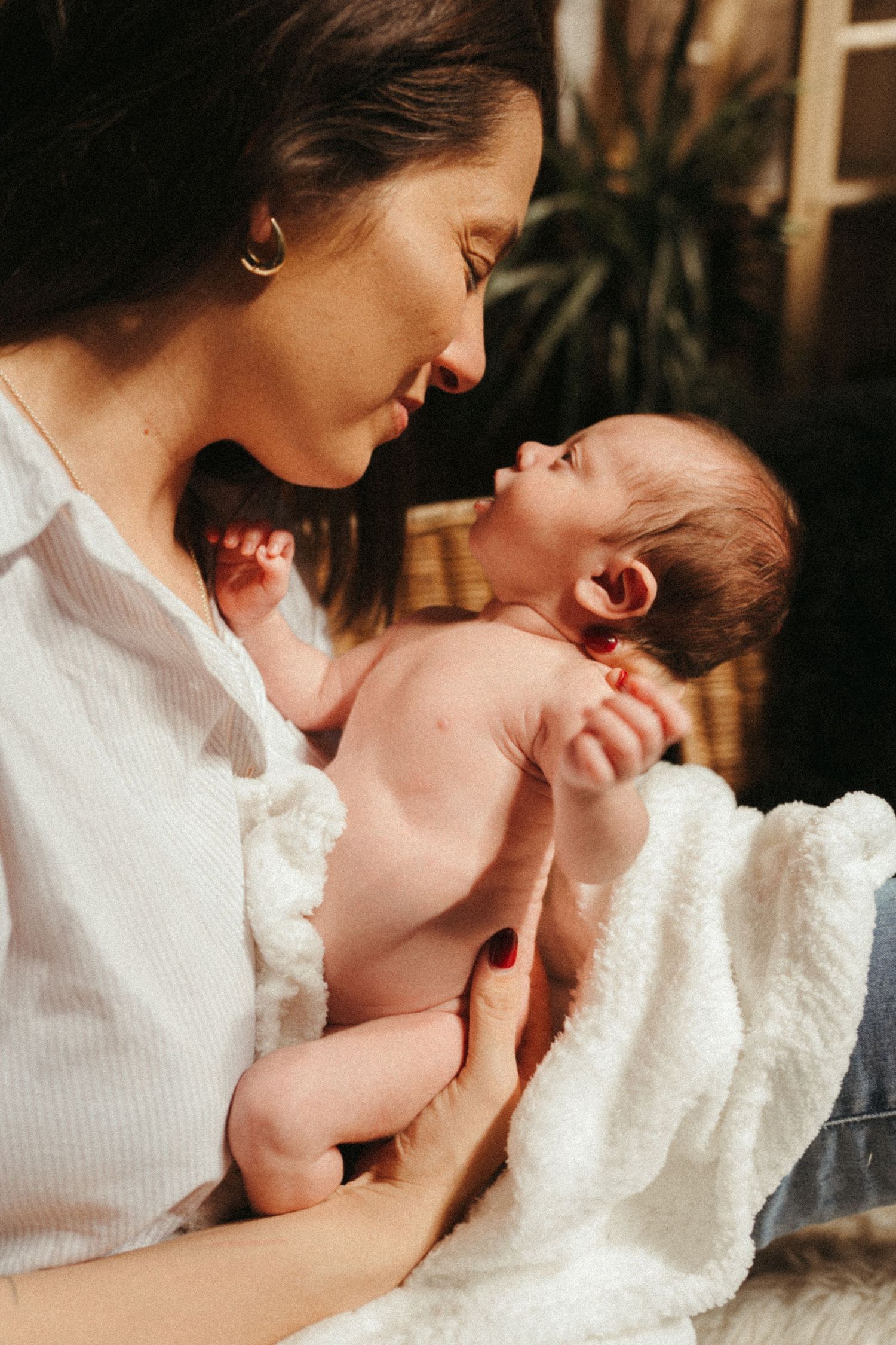 Parent in white shirt sharing affectionate moments with baby on white blanket.