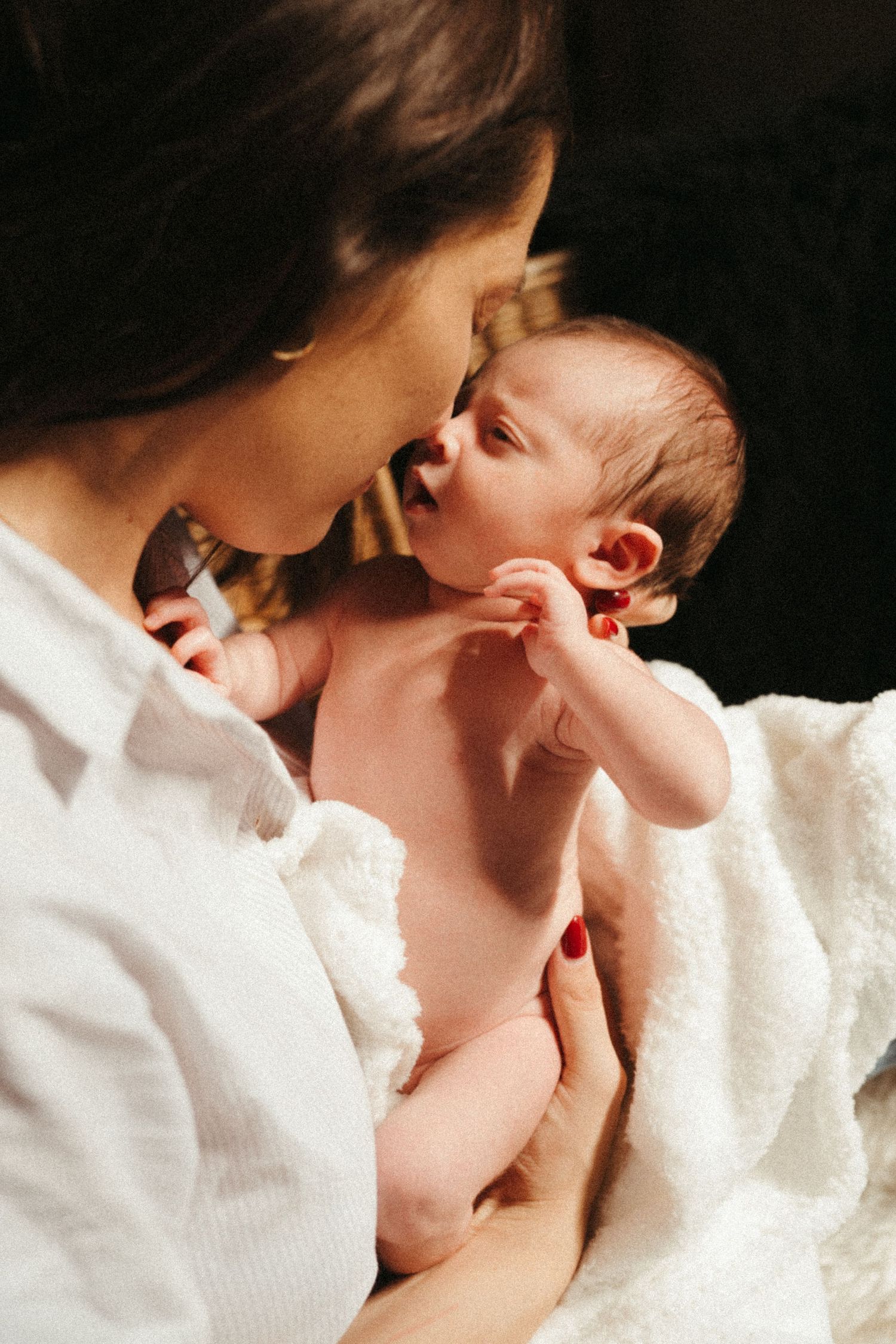 Intimate black and white portrait of parent cradling and kissing newborn.