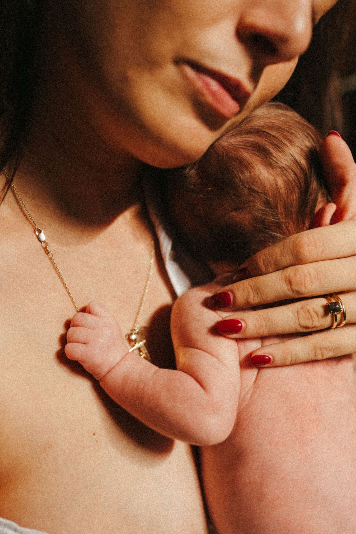 Close-up of hands with red nails and jewelry gently cradling baby.