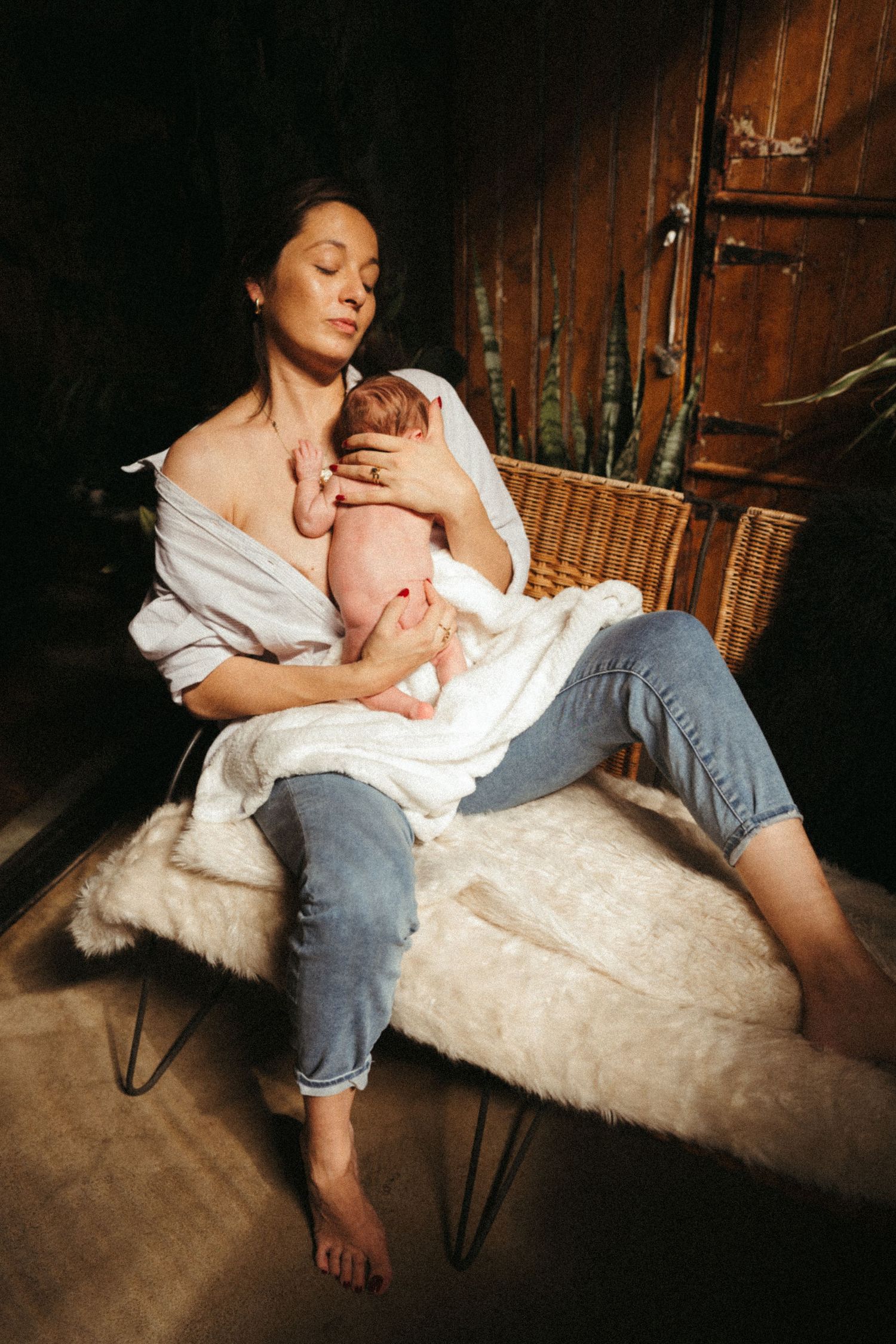 Parent in white shirt reclining with baby on furry chair in atmospheric lighting.