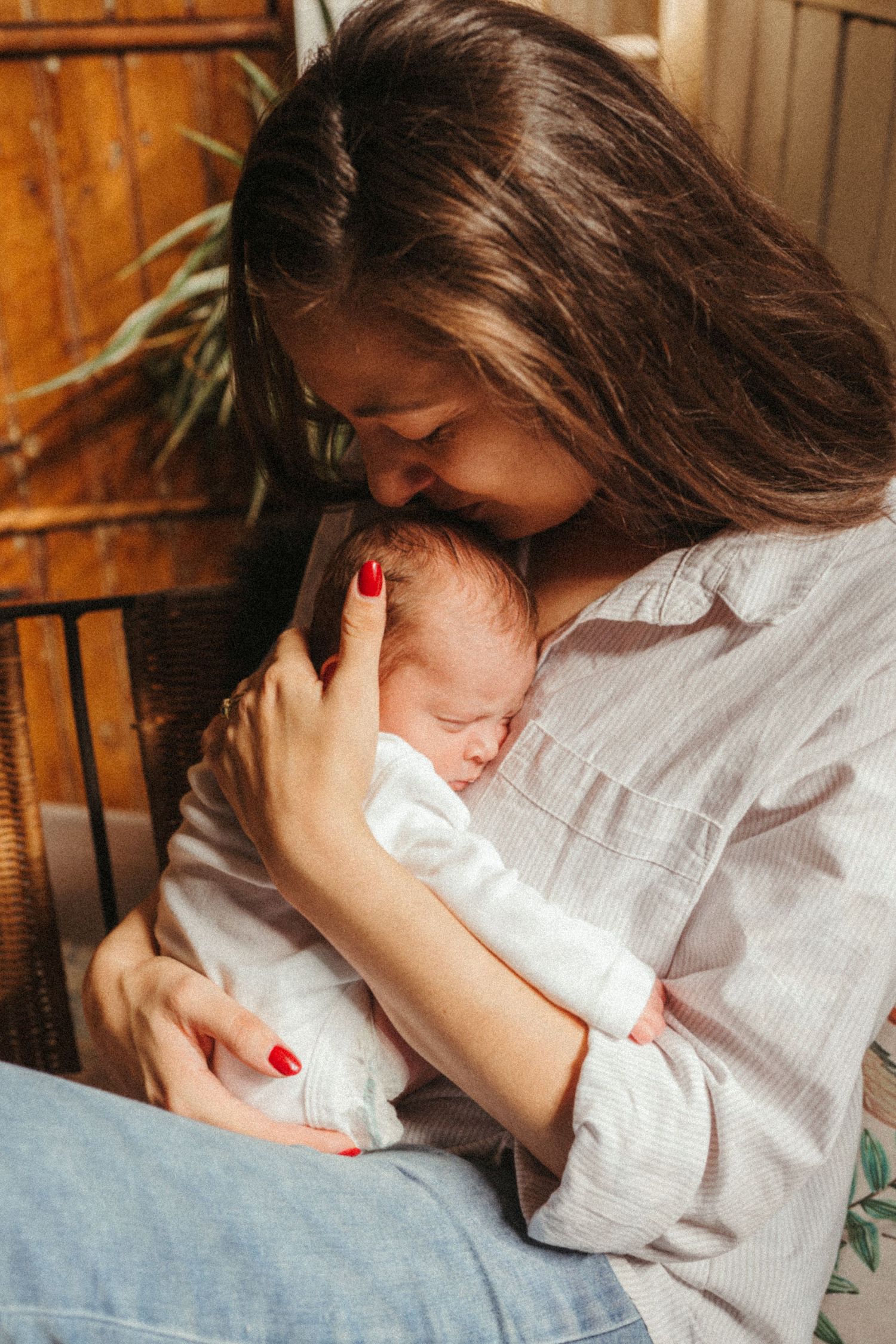 Mother in white shirt tenderly holding sleeping newborn on soft bedding.