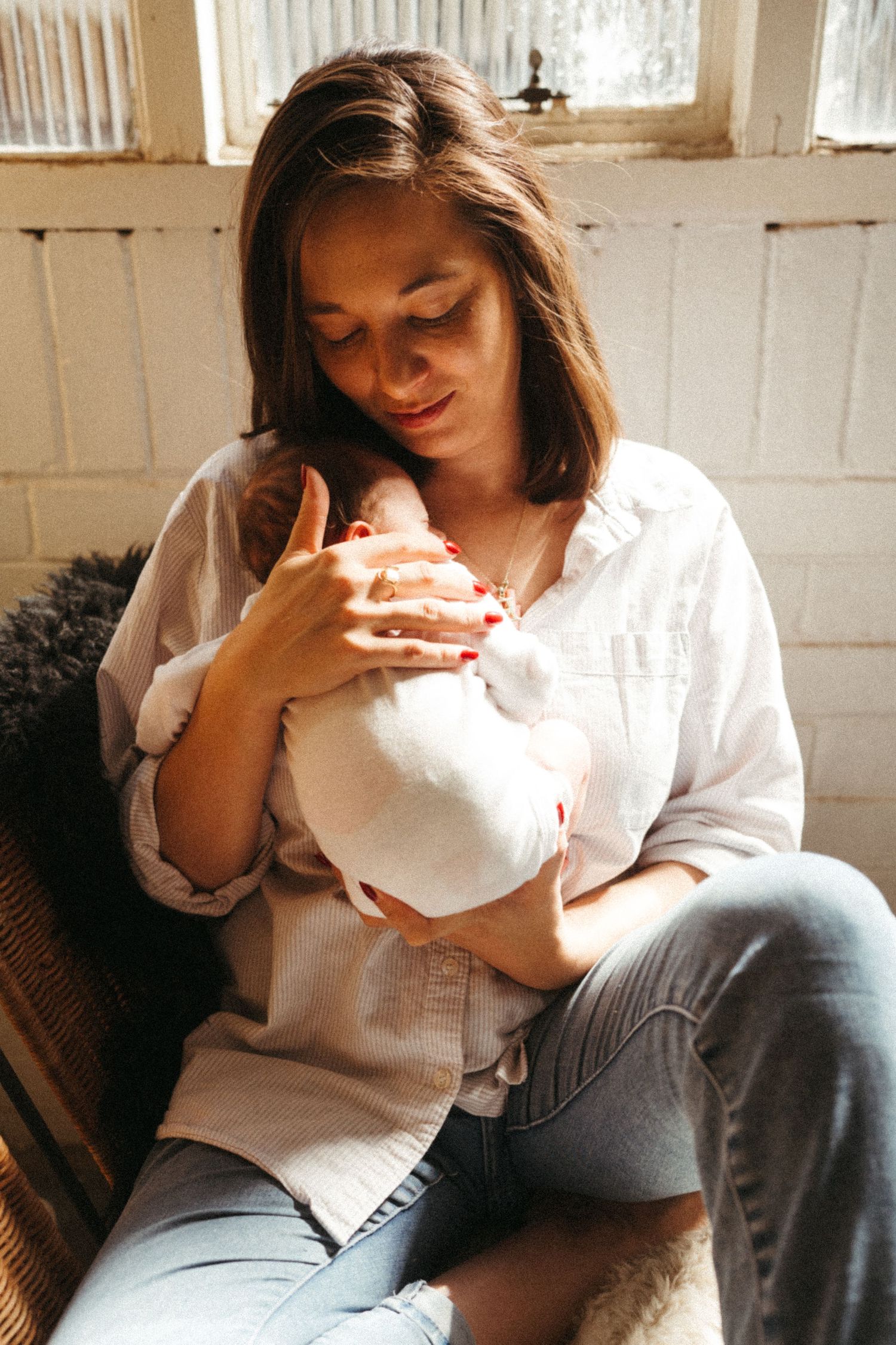 Mother in casual attire bonding with newborn in sunlit room.