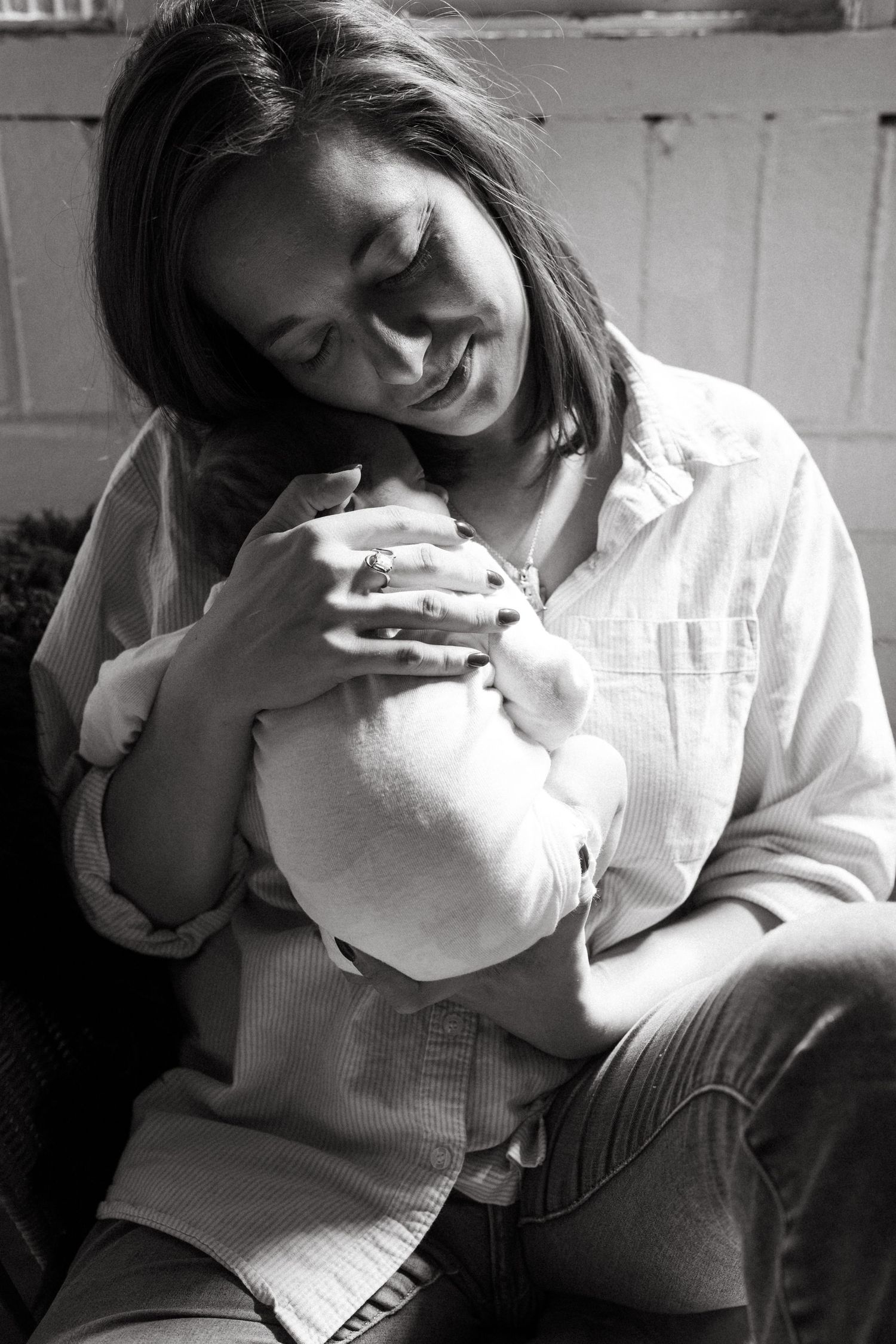 Mother in white shirt cradling newborn baby in natural window light.