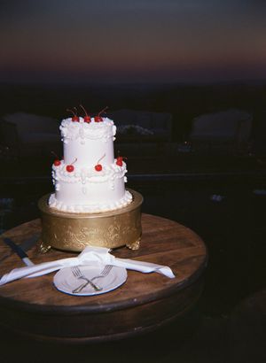 Two wedding cakes on wooden stands, one white with red accents and one with gold metallic finish.