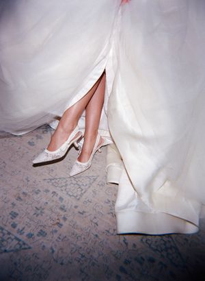 White bridal shoes peek out from beneath the hem of a flowing wedding dress.