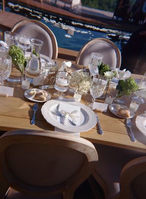 Elegant table settings with white floral centerpieces and crystal glassware arranged on a wooden table for a wedding reception.