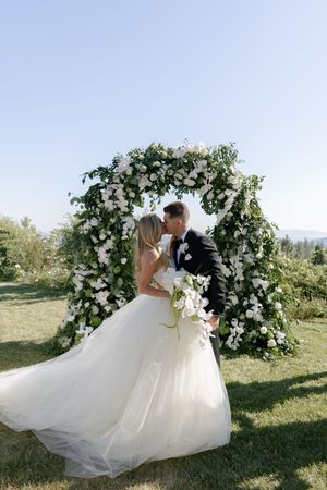 Romantic wedding couple shares intimate moments under a floral arch in an outdoor garden setting.