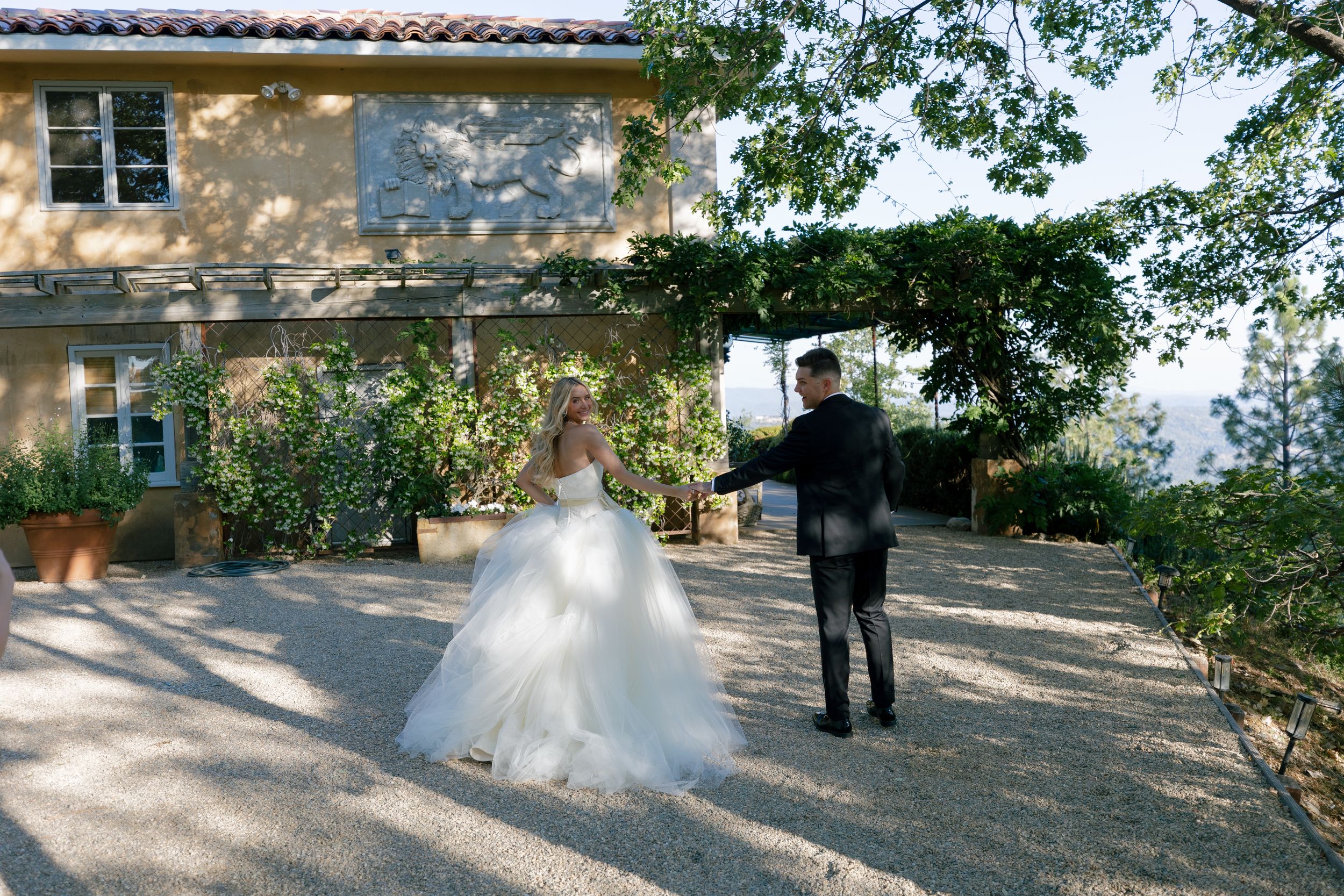 Elegant wedding scene at a Mediterranean villa with couple walking on gravel path.