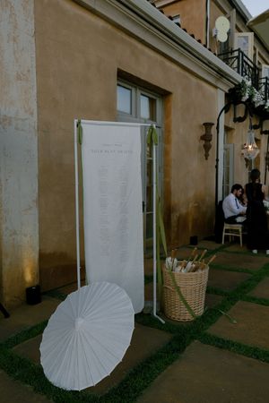 White parasol and event details sign displayed outside a beige building entrance.