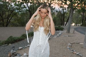 Woman in white lace dress walking along a scenic mountain trail at sunset.