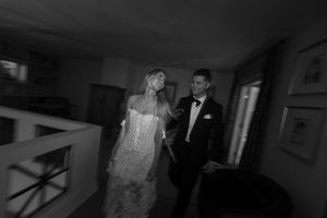 A couple in formal wedding attire walks through a dimly lit hallway.