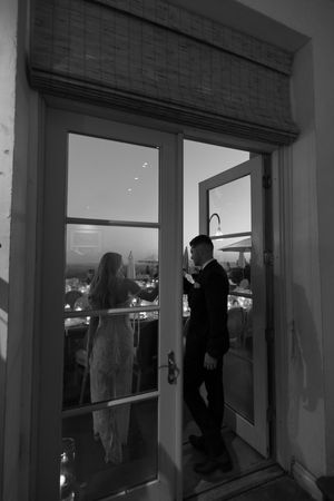 Silhouettes stand against large windows at dusk creating a moody atmosphere.
