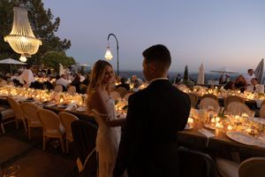 Elegant outdoor wedding reception tables with glowing candles and floral centerpieces at sunset overlooking the ocean.