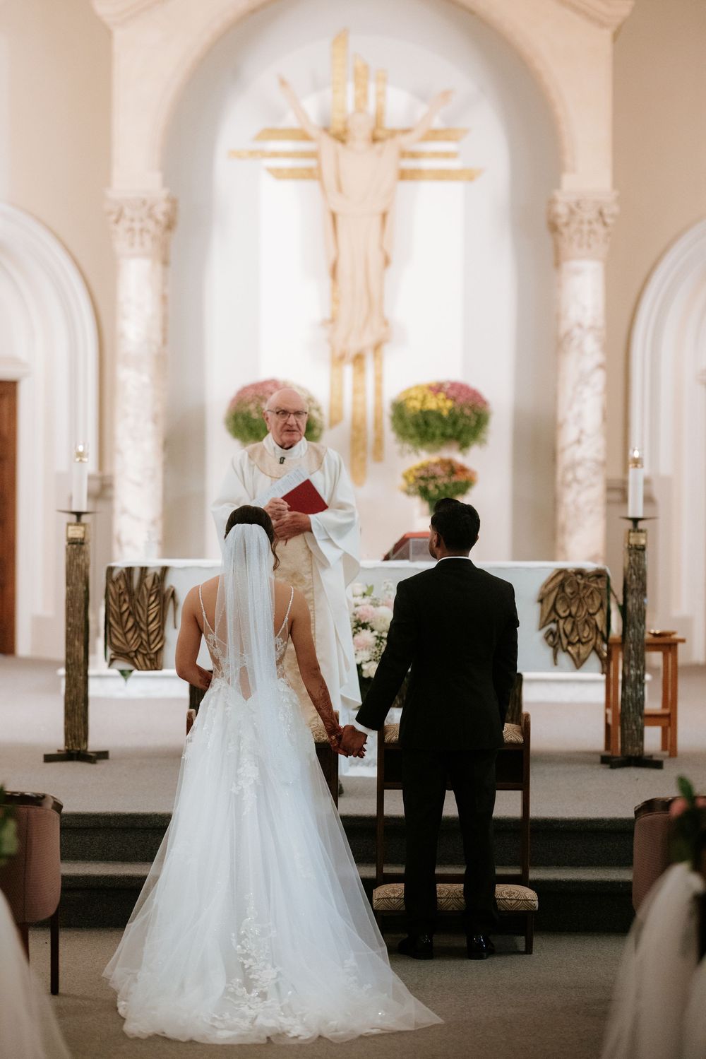 A wedding ceremony in a bright white church interior with ornate columns and arches.