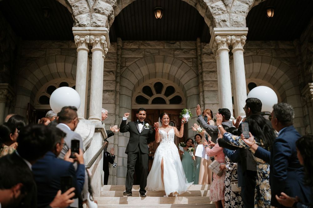Wedding ceremony guests mingle beneath stone archways and columns in a historic building.
