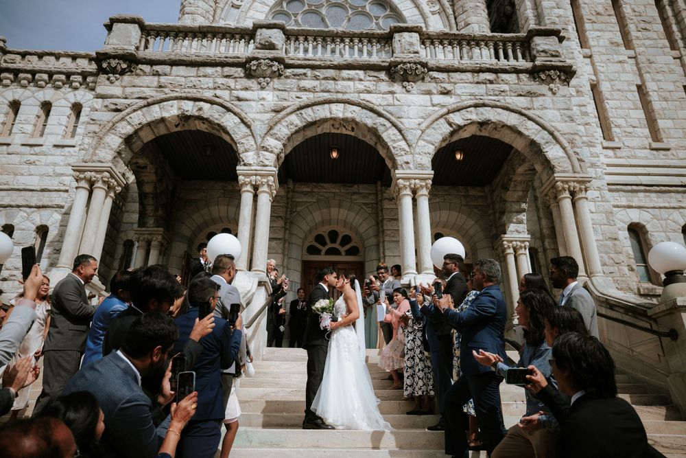 Wedding guests gather outside an ornate stone building with arched doorways during an elegant celebration.