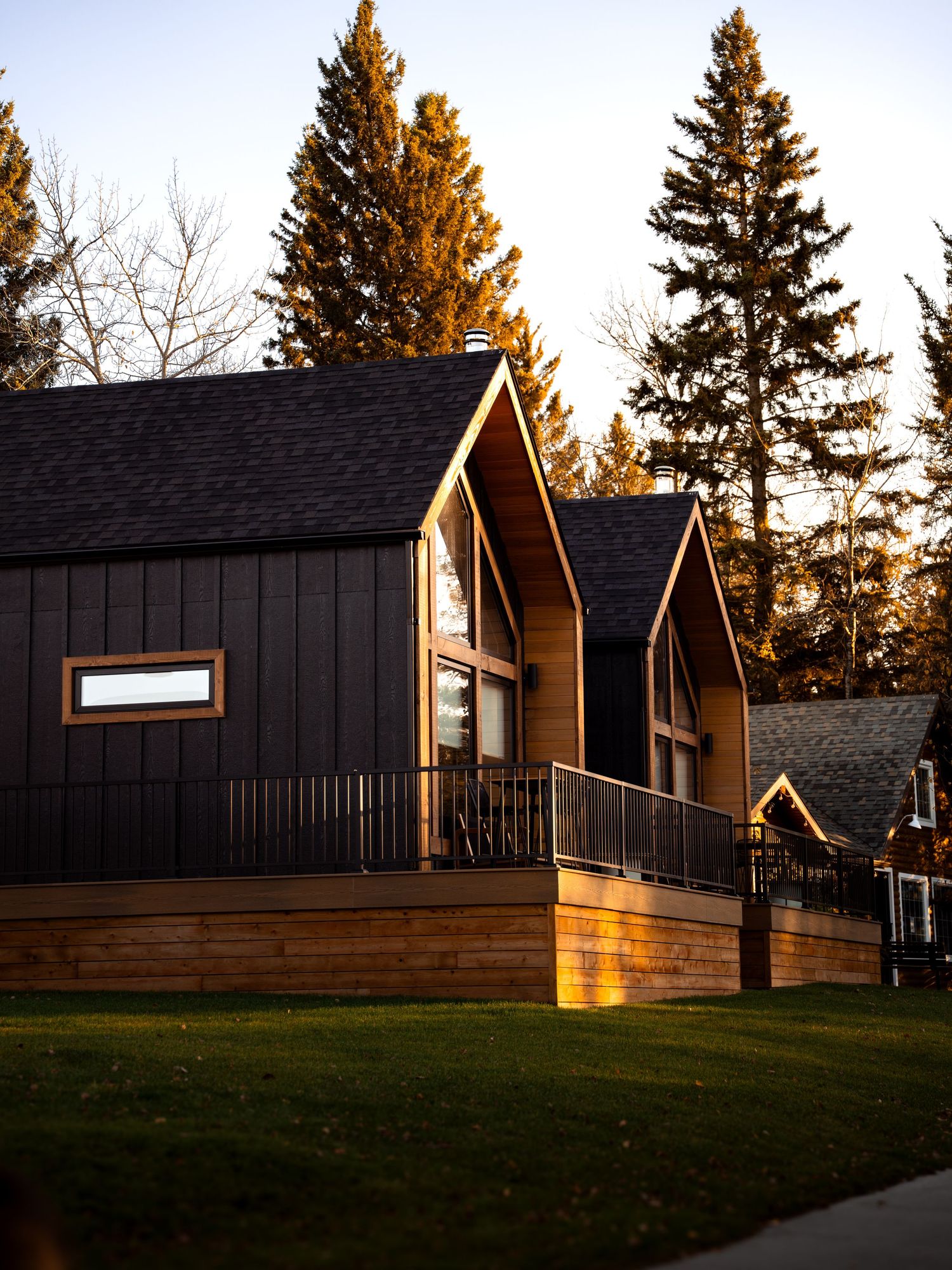 Modern black cabin-style homes with wooden decks illuminated by golden sunset light.