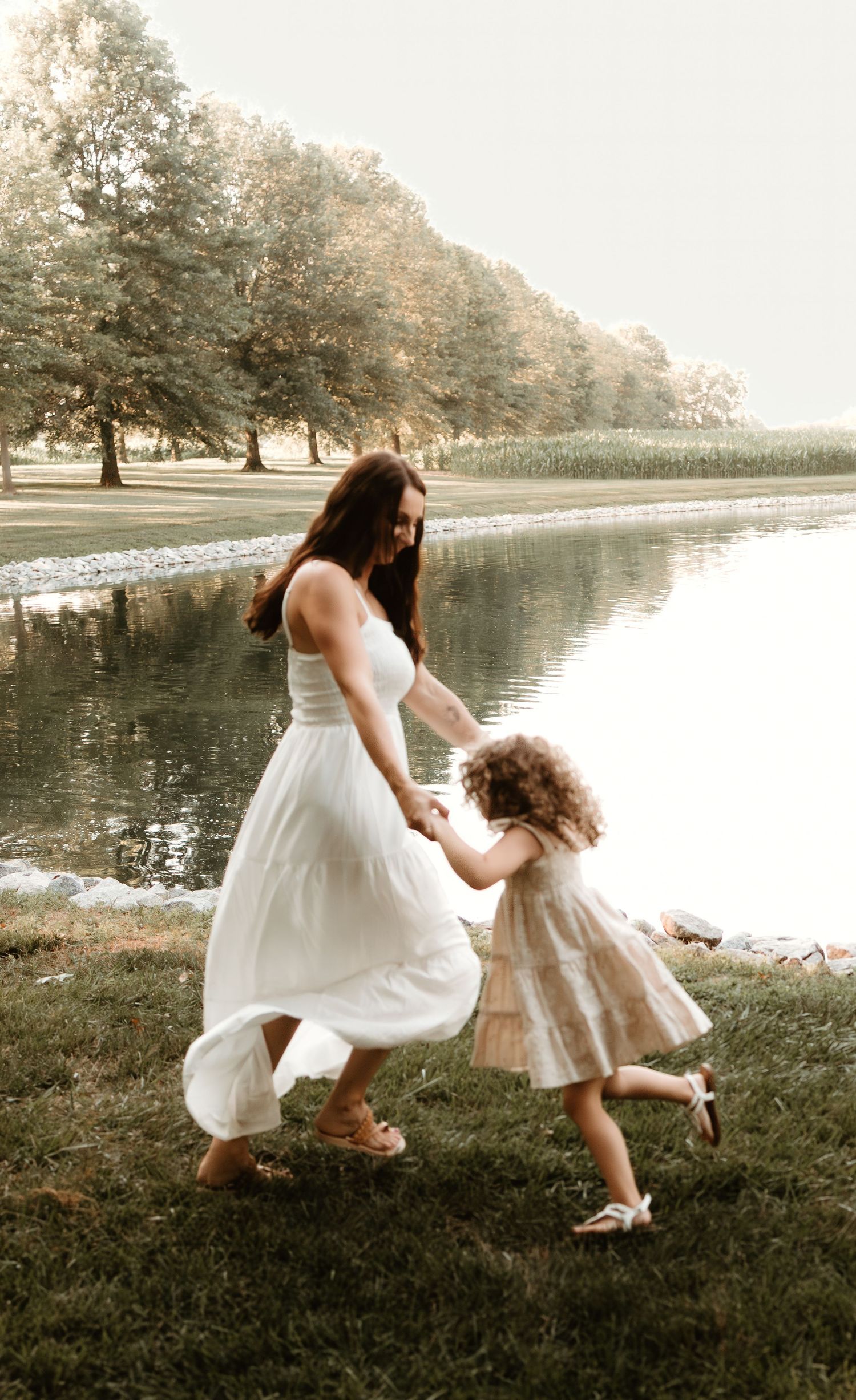 Dancing together by lakeside in flowing white dresses during golden hour.