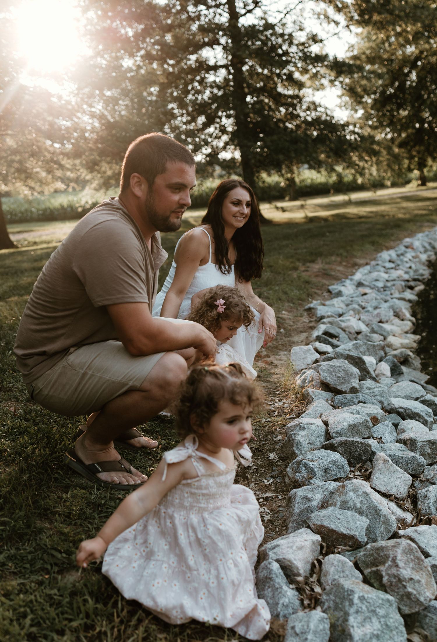 Family shares tender moment together on rocky lakeside during sunset.