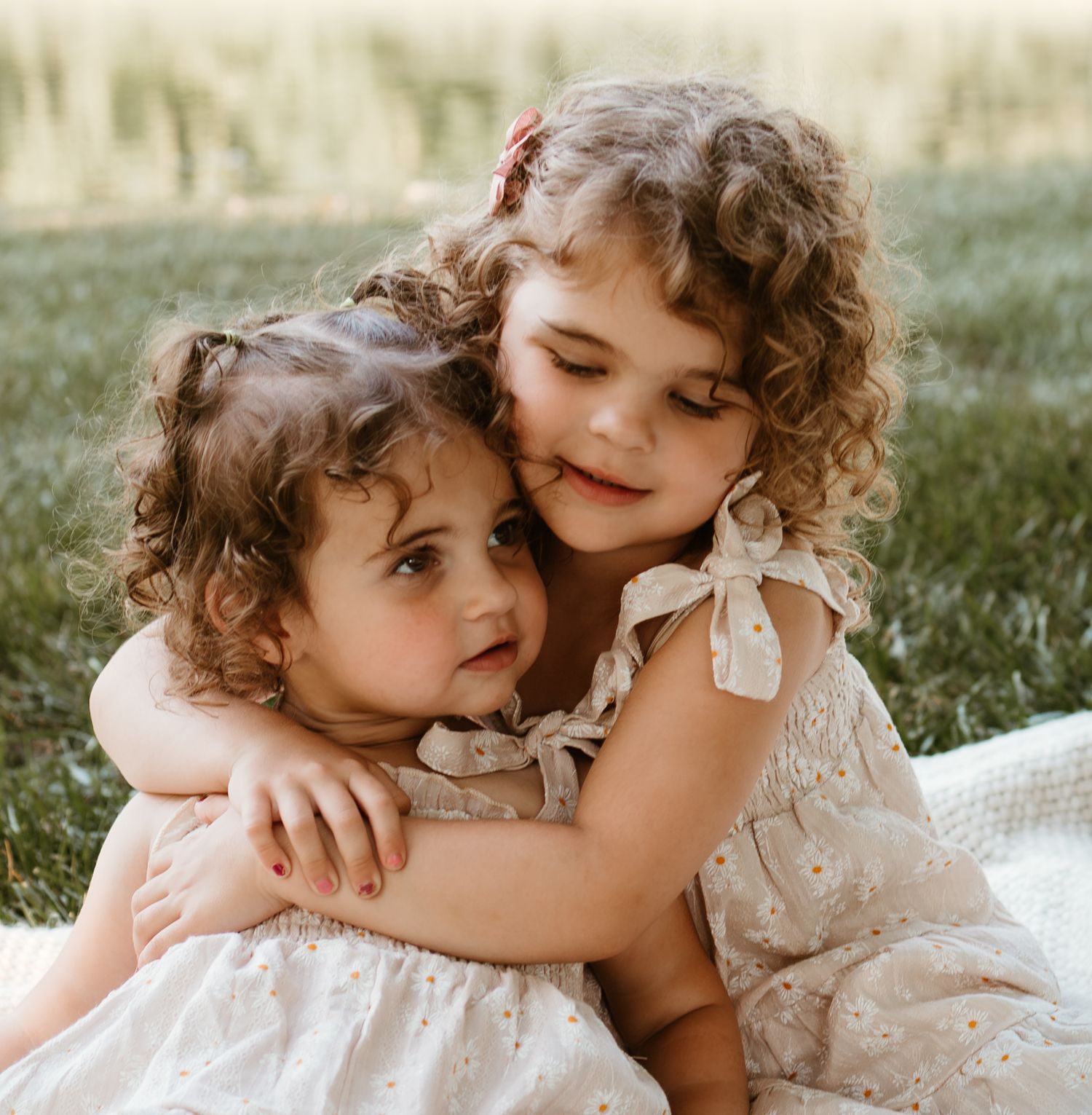 Two young children in white dresses share a sweet embrace while smiling.