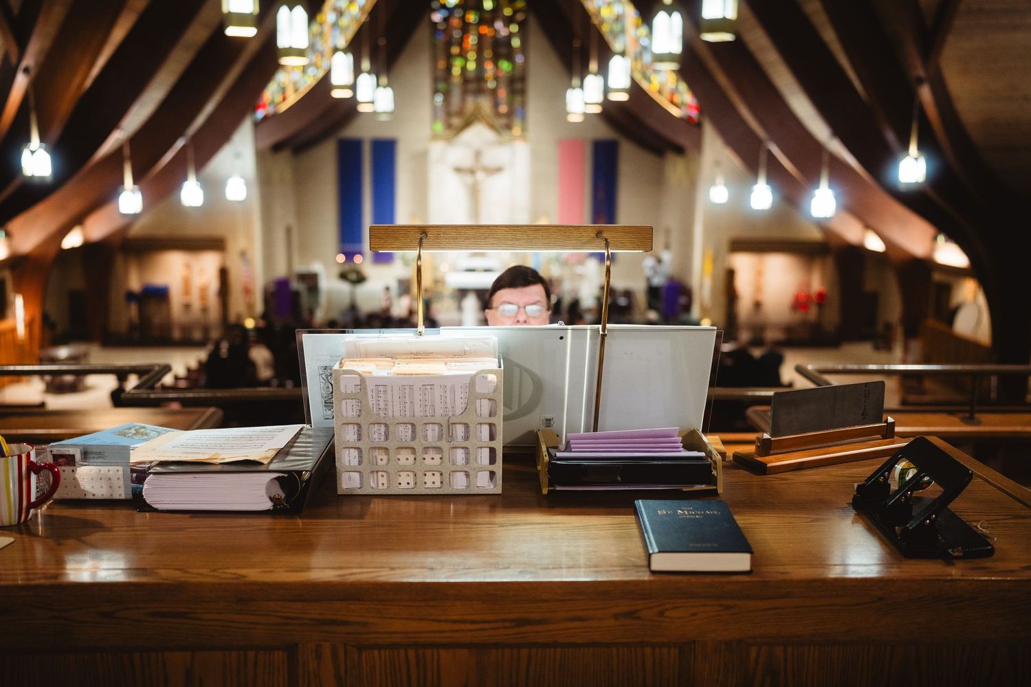Modern church interior with wooden beams, stained glass windows, and rows of empty pews illuminated by warm lighting.