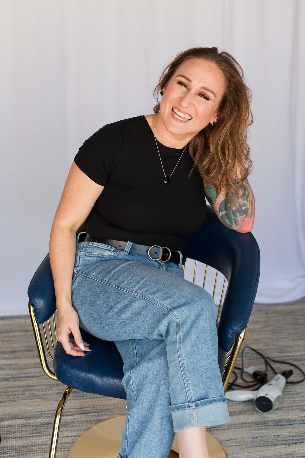 Casual portrait showing relaxed smile while seated in modern blue styling chair.